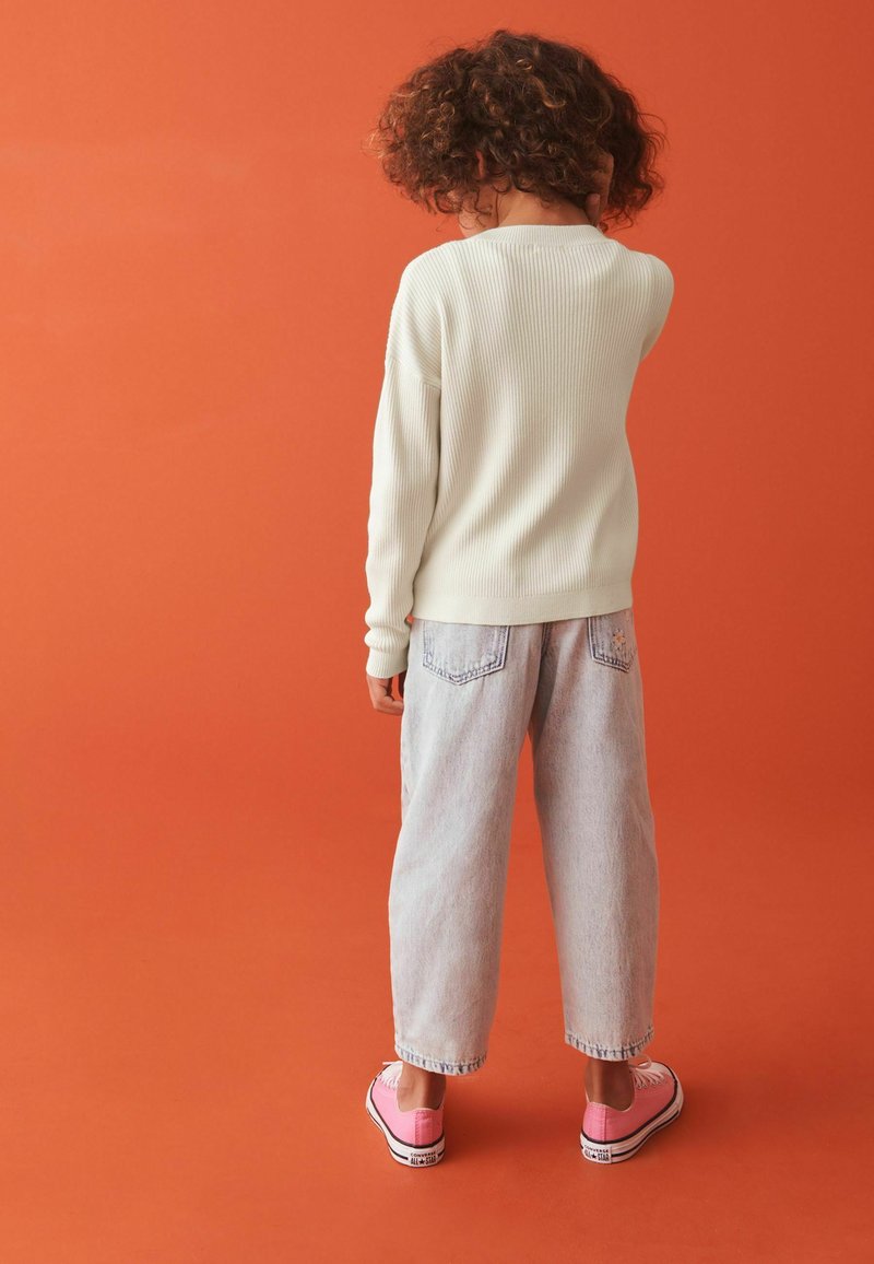 Cremefarvet ribstrik sweater, lyseblå baggy jeans og lyserøde sneakers. Baggrunden er én ensfarvet orange farve.