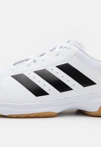 Zapatilla deportiva blanca con un upper texturizado, que presenta tres franjas negras audaces, una suela de goma y cordones blancos.
