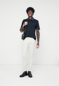 Námornícky polo tričko s kontrastným golierom a manžetami, v kombinácii s bielymi slim-fit nohavicami a čiernymi koženými topánkami. Súčasťou je aj malá ramenná taška.