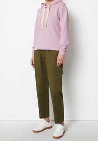 Sudadera con capucha de color rosa claro con cordones de crema, combinada con pantalones cargo verdes oliva que cuentan con bolsillos laterales. Llevada con zapatillas blancas.