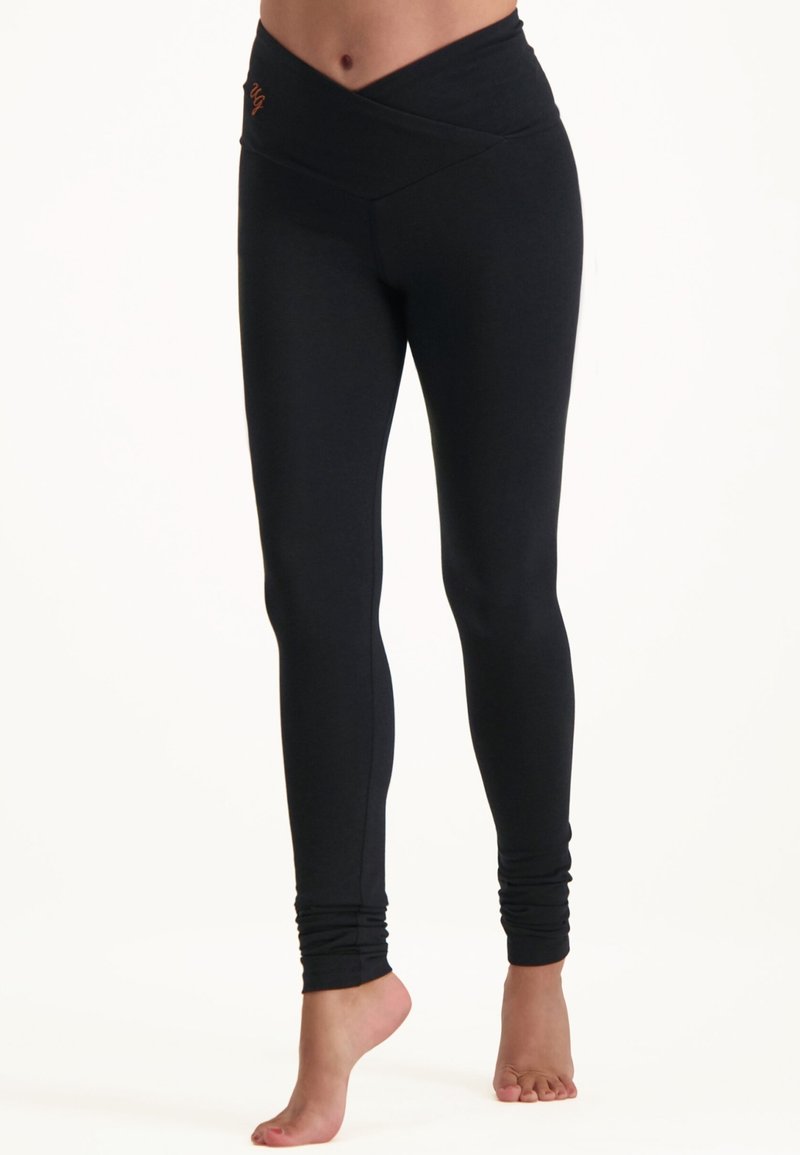 Schwarze Leggings mit einem überkreuzten Bunddesign. Hergestellt aus dehnbarem Stoff, mit glatter Textur und Bündchen-Detail an den Knöcheln.