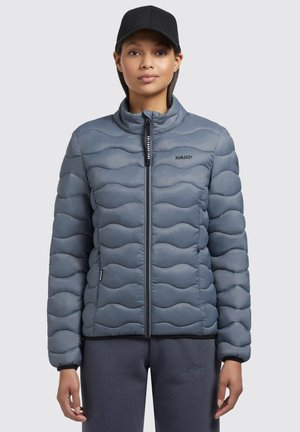 Grijze pufferjack met een golfpatroon gequilt textuur, hoge kraag en ritssluiting. Zwart logo op de borst, gecombineerd met grijze onderstukken.