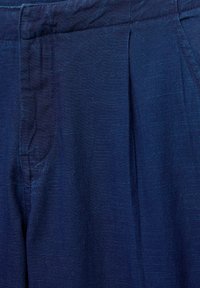 Close-up van donkerblauwe stoffen broeken met zichtbare voorplooien en stiksels van de tailleband.