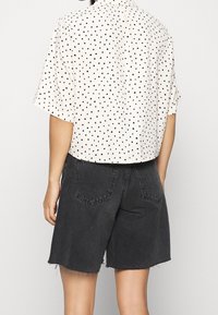 Blusa blanca con lunares, de manga corta, combinada con pantalones cortos de mezclilla negros de cintura alta, con un dobladillo deshilachado y bolsillos con parche.