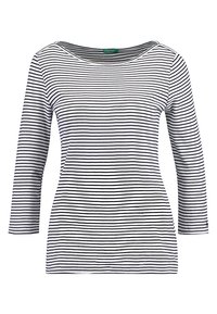 Långärmad topp i vit bomull med tunna svarta horisontella ränder. Har en vid halsringning och åtsittande ärmar. Slät textur.