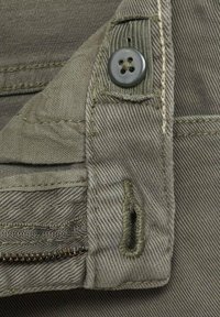 Tessuto di cotone verde oliva con cuciture visibili. Presenta una chiusura con bottone, una tasca con zip e una superficie testurizzata.