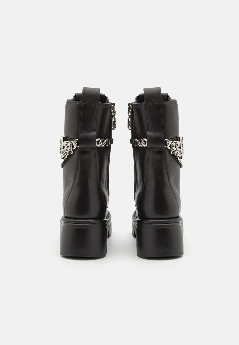 Schwarze Lederstiefel bis zur Wade mit dicken Sohlen, silberner Kette und Schnallenakzenten um die Knöchel, von hinten auf einem weißen Hintergrund gezeigt.