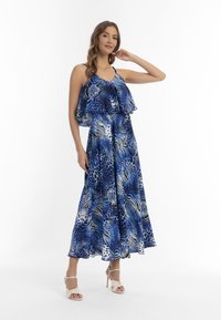 Rochie albastră cu un design tipărit, având un bust stratificat; prezintă imprimeuri abstracte cu animale și o siluetă fluidă, completată de tocuri bej cu bretele.