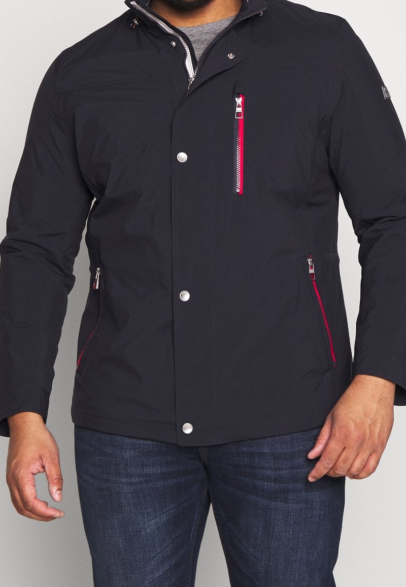 Námořnická nepromokavá bunda s červenými zipy, stříbrnými cvočky a bočními kapsami. Obsahuje stojáček a hladkou texturu látky.