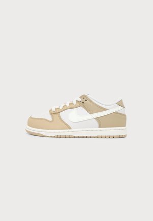 Low-Top Sneaker mit beigen und weißen Lederpaneelen, weißen Schnürsenkeln und einem weißen Swoosh-Logo an der Seite vor einem einfarbigen Hintergrund.
