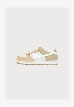 Basket basse avec panneaux en cuir beige et blanc, lacets blancs et logo blanc Swoosh sur le côté, sur un fond uni.