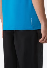 Modré sportovní tričko s hladkou texturou, kombinované s černými šortkami se bočními švy. Malé logo "FLASHDRY XD" na lemu trička.