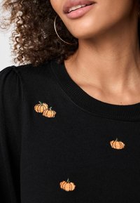 Maglione nero con scollo rotondo, decorato con zucche arancioni ricamate, che presenta un motivo in maglia testurizzata e leggere maniche a sbuffo.