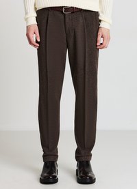 Braune, plissierte Hose aus strukturiertem Stoff. Am Bund mit einem braunen Gürtel eng anliegend, in Knöchellänge, kombiniert mit schwarzen Schuhen.