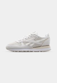 White sneaker with suede and mesh materials, rounded shape, lace-up design, and a rubber sole. Features tonal accents and perforated detailing.