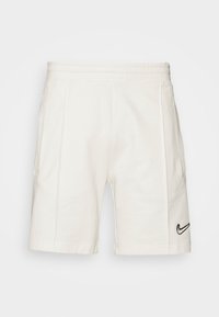 Nike shorts in cream color, made of soft fabric. Features an elastic waistband and black logo accent on the right side. Plain design.