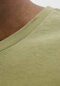 Korte mouwen shirt in licht olijfgroen katoen, met een fijne geribbelde halslijn en een gladde textuur, die een close-up van de stiksels toont.