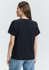 T-shirt en coton bleu marine avec des manches courtes, un col rond et une coupe décontractée, associé à un jean bleu clair. Texture lisse, design simple.