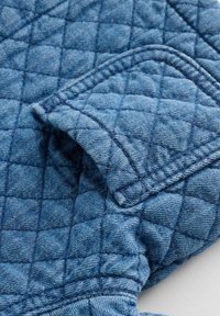 Gequiltede blauwe denimstof met een geruit patroon, voorzien van een gestructureerd oppervlak en zichtbare stiksels langs de randen.