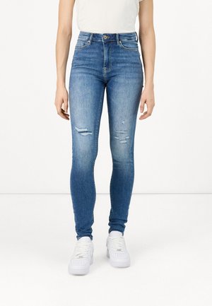 Skinny blue jeans made of denim, featuring a high waist, slight whiskering, and distressed details. Paired with white sneakers.