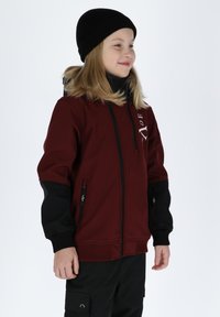 Maroon jacket with black accents, zippered pockets, and a high collar. Soft texture and flexible fit, worn with a black beanie.