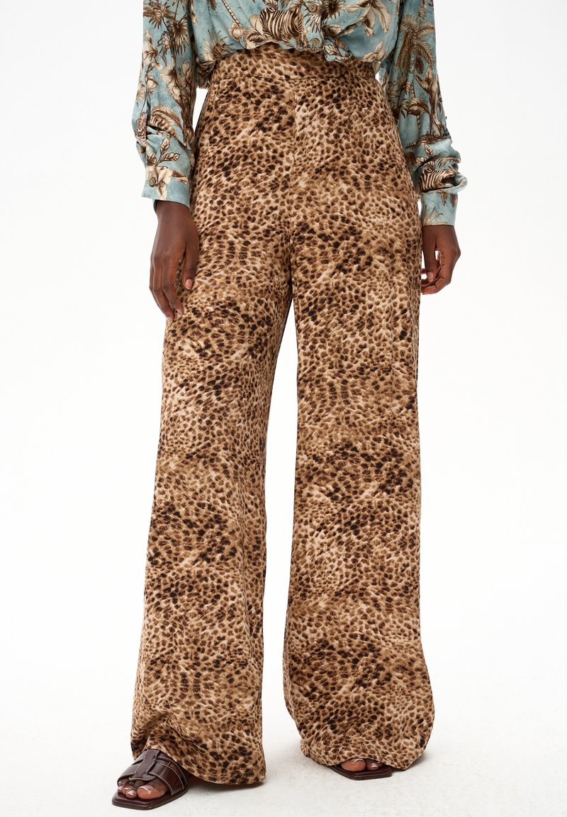 Wijde broek met bruin-zwarte luipaardprint, gecombineerd met donkere sandalen en een blauw gemêleerd shirt met lange mouwen, zichtbaar van taille tot voeten.