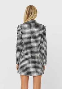 Blazer a motivo houndstooth bianco e nero con maniche lunghe, colletto classico e vestibilità sartoriale, con una fessura sul retro per facilitare i movimenti.