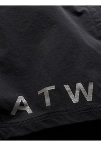 Czarna tkanina o miękkiej fakturze z dużymi, odbijającymi światło srebrnymi literami piszącymi "ATW" w pobliżu dolnej krawędzi. Czysty, minimalistyczny design.