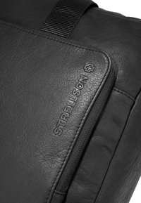 Borsa nera in pelle con una superficie texturizzata, dotata di chiusura con zip e dettaglio del logo impresso. Include una tracolla resistente per il trasporto.