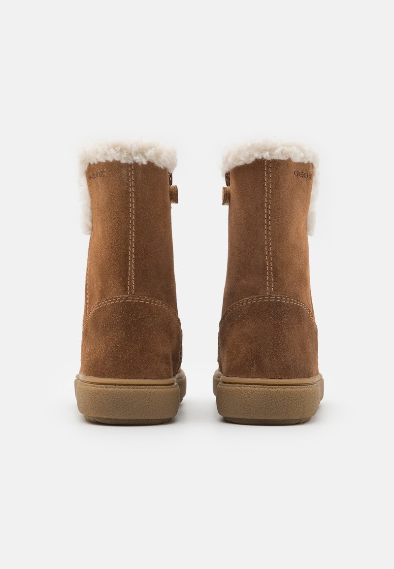 Braune Wildleder-Stiefeletten mit einem weißen Kunstfellaufschlag, flacher Gummisohle und subtilen Nähten auf der Rückseite. Geox-Logo an der Seite.
