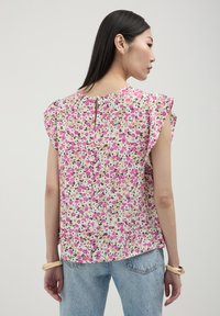 Blusa floreale in tessuto leggero con fiori rosa e viola. Presenta maniche a sbuffo corte e un dettaglio a chiave sul retro. Vestibilità casual.