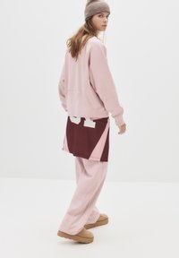Różowy, oversize'owy sweter z prążkowanymi mankietami, zestawiony z burgundowymi szortami w kolorowe bloki. Beżowe buty bez zapięcia dopełniają stylizację.