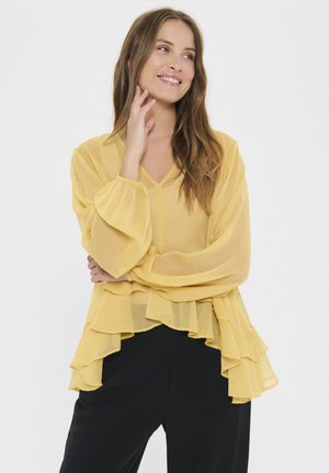 Yellow chiffon blouse with voluminous long sleeves and layered ruffle hem. V-neck design complements the lightweight, flowing fabric.