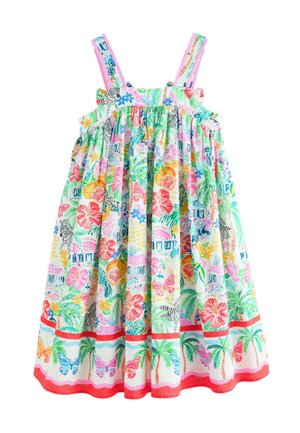 Ung pige står iført en farverig sommerkjole med tropiske og sommerfugleprint samt hvide sandaler med farverige stropper.