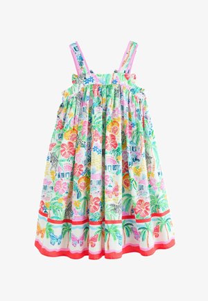 Ung pige står iført en farverig sommerkjole med tropiske og sommerfugleprint samt hvide sandaler med farverige stropper.