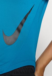 Blaues Sportshirt aus strukturiertem Stoff mit einem großen schwarzen Nike-Swoosh-Logo an der Seite und einem schwarzen Bund.