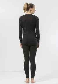 Svart långärmad topp och figurnära leggings i ett mjukt, ribbat tyg. Toppen har en rundad halsringning och leggingsen smalnar av vid anklarna.
