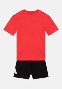 Röd bomull T-shirt med korta ärmar och rundad halsringning, kombinerad med svarta shorts med en vit triangelaccent på sidan.