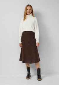 Gebreide trui in off-white met een hoge kraag, gecombineerd met een bruine A-lijn midi-rok. Zwarte enkellaarsjes met een dikke zool.