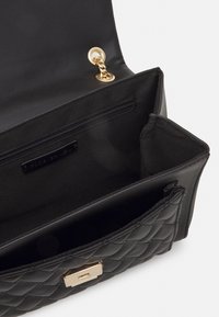 Czarna pikowana torebka z gładkim wnętrzem, złotymi elementami, kieszenią na zamek błyskawiczny i z magnetycznym zapięciem. Posiada detal w postaci łańcuszka.