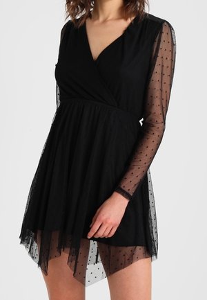 Black dress with a wrap design, featuring sheer dotted long sleeves and a layered skirt. Fabric shows slight sheerness with a textured appearance.