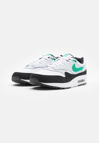 Baskets en cuir blanc et suède noir avec un swoosh Nike vert, lacets ronds, col rembourré et une unité d'air visible dans la semelle.