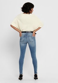 Skinny blue jeans made of denim, featuring a mid-rise waist, two back pockets, and a faded wash, paired with a cream-colored top.