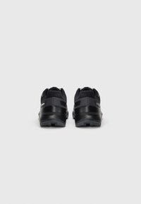 Pair of black athletic shoes with rugged soles, viewed from the back on a plain light background.