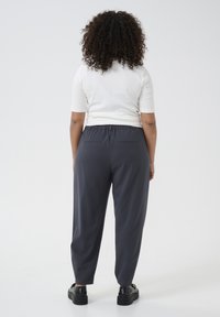 Dunkelgraue, lässig geschnittene Hose mit elastischem Bund und zwei Gesäßtaschen, kombiniert mit einem kurzärmeligen weißen Oberteil. Flache Schuhe sind sichtbar.