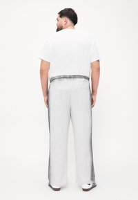 Lyse grå joggebukser med elastisk midje og baklomme, sammen med en enkel hvit t-skjorte. Glatt stoffstruktur.