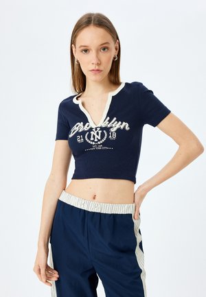 Marineblauw cropped T-shirt met een V-hals, geribbelde textuur, crèmekleurige accenten en bedrukte "Brooklyn"-ontwerp; gecombineerd met marineblauwe broek met gestreepte tailleband.