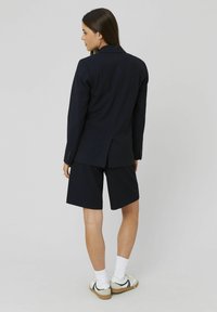Veste de costume à rayures navy assortie avec un short. La veste présente un col cranté et deux boutons ; le short est droit.