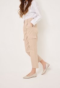 Pantalons cargo beiges avec poches latérales, présentant une jambe fuselée ; assortis à des ballerines en cuir verni clair avec découpes et détails sur les orteils.