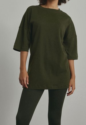 Olivgrünes, übergroßes T-Shirt aus weichem Stoff mit rundem Ausschnitt und kurzen Ärmeln, kombiniert mit passenden, strukturierten Leggings.